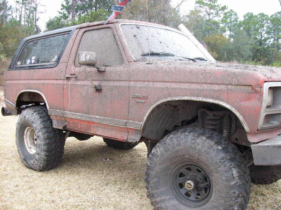 Mud-covered 1986 Ford Bronco with large tires, 3/4 front view
