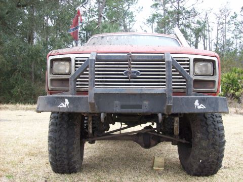 1986 Ford Bronco - This lifted Ford truck features a heavy-duty aftermarket bumper with decorative decals and a prominent flag.