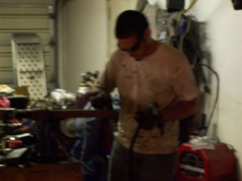 1986 Ford Bronco - A man is seen working on machinery in a garage setting with various tools and items around him.