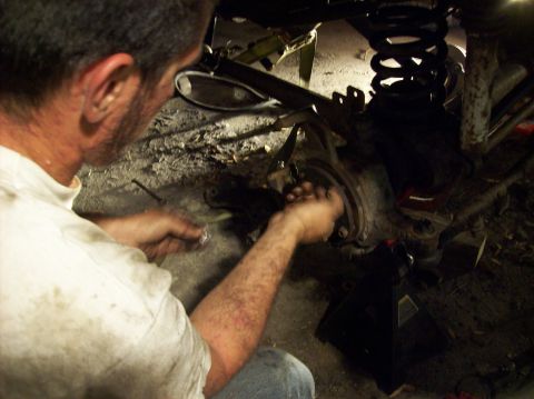 1986 Ford Bronco - A mechanic is shown working on the suspension of a vehicle, with a coil spring and other components visible.