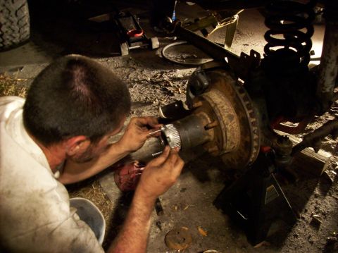1986 Ford Bronco - A mechanic performs maintenance on the front hub assembly of a vehicle, with tools and parts scattered around.