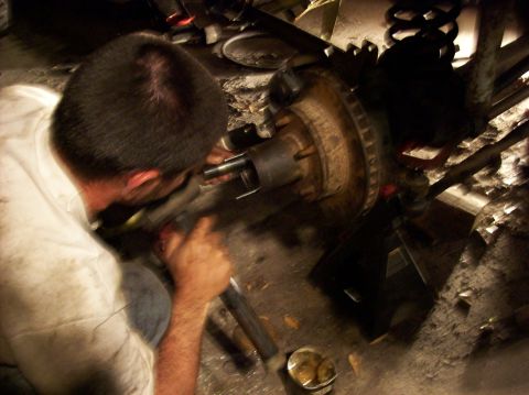 1986 Ford Bronco - Mechanic works on a vehicle's brake rotor and hub assembly, likely during a repair or maintenance procedure.