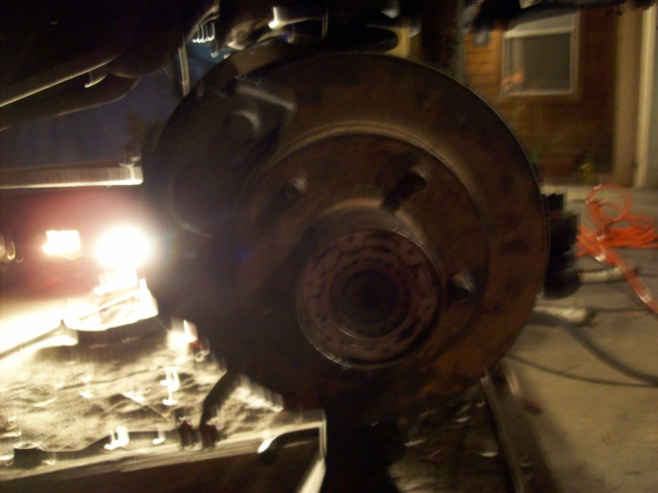 close-up of vehicle's front brake rotor and suspension parts, with a bright light illuminating the area