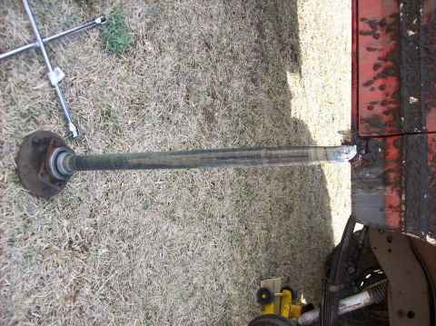 1986 Ford Bronco - A driveshaft is shown on the ground, next to a red surface and some grass.