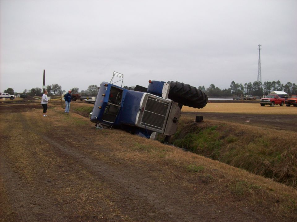 Blue tractor overturned on its side in a ditch, with large rear tire visible