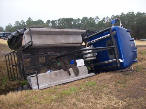 1986 Ford Bronco - A blue semi-truck and its trailer have overturned, resting on its side in a grassy ditch.