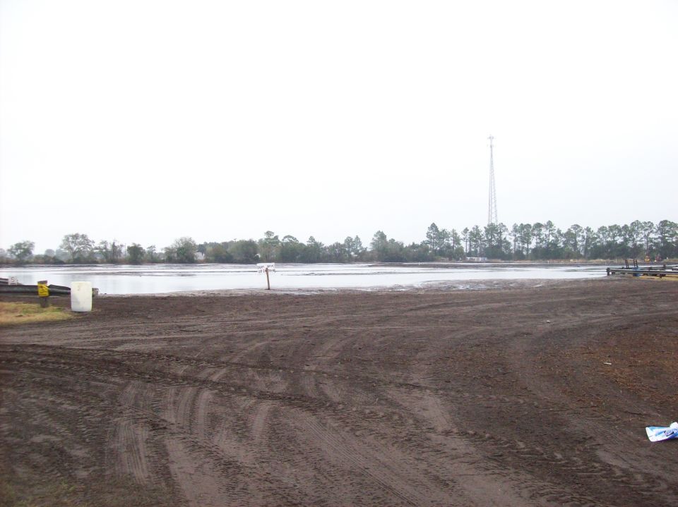 muddy area next to a lake with trees and a tower in the distance