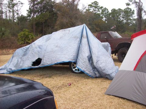 1986 Ford Bronco - A tarp covers a vehicle, with a red pickup truck and a tent visible in the background.