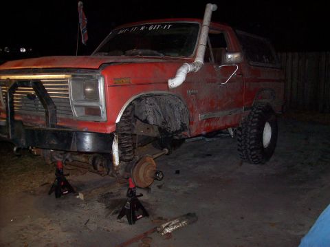1986 Ford Bronco - Red SUV on jack stands with snorkel and brush guard, undergoing maintenance.