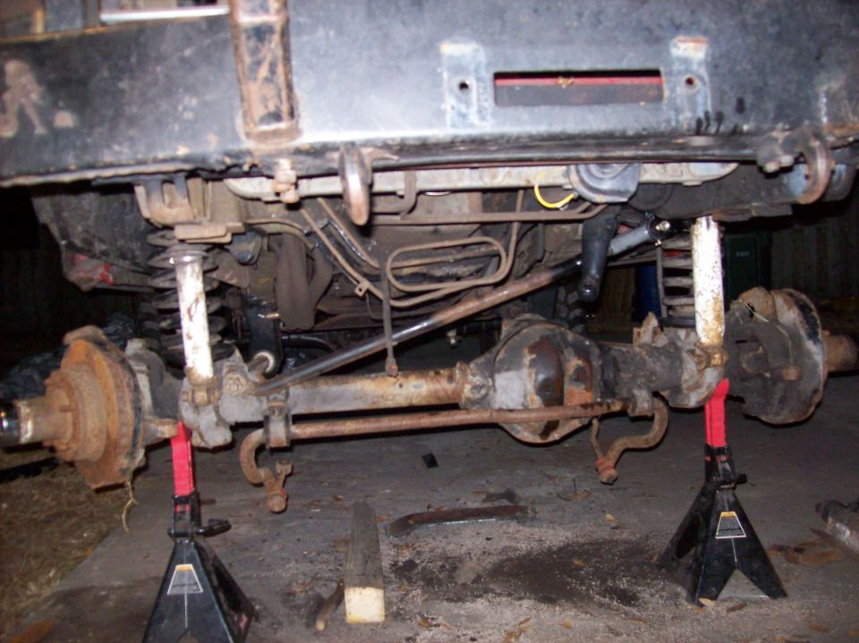 Undercarriage of a vehicle on jack stands, showing axles, suspension, and exhaust components