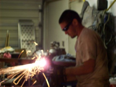 1986 Ford Bronco - A man in sunglasses works with a welding torch, creating a shower of sparks in a garage setting.