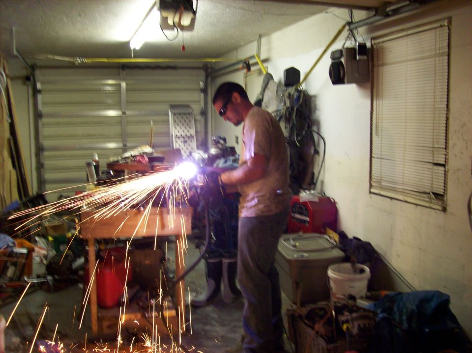 man welding with sparks flying in a cluttered garage