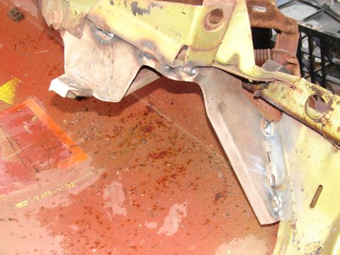 1973 Ford Ranchero - Close-up of body-repair welding on a red-oxide primered floor pan, where a new bare-steel patch and gusset are stitch-welded to yellow-pain…