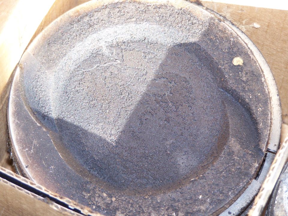 Piston with carbon buildup and a visible crack, resting in a cardboard box