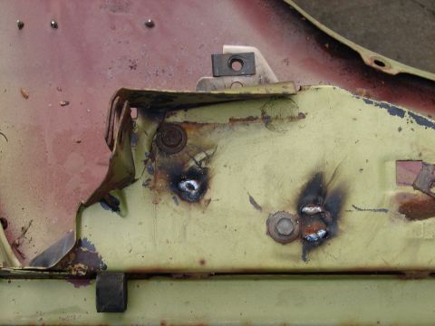 1973 Ford Ranchero - Extreme close-up of pale green sheet metal during body repair, showing fresh plug welds burned through the panel with scorched heat-discolo…