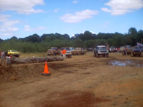 1976 Ford F-100 - Mud drag racing event with multiple trucks on a dirt track. A large log is in the foreground.
