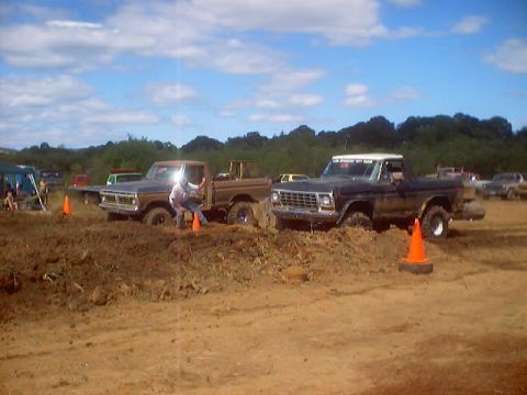1976 Ford F-100 - Two Ford F-100 trucks are stuck in the mud during a competition on a sunny day.