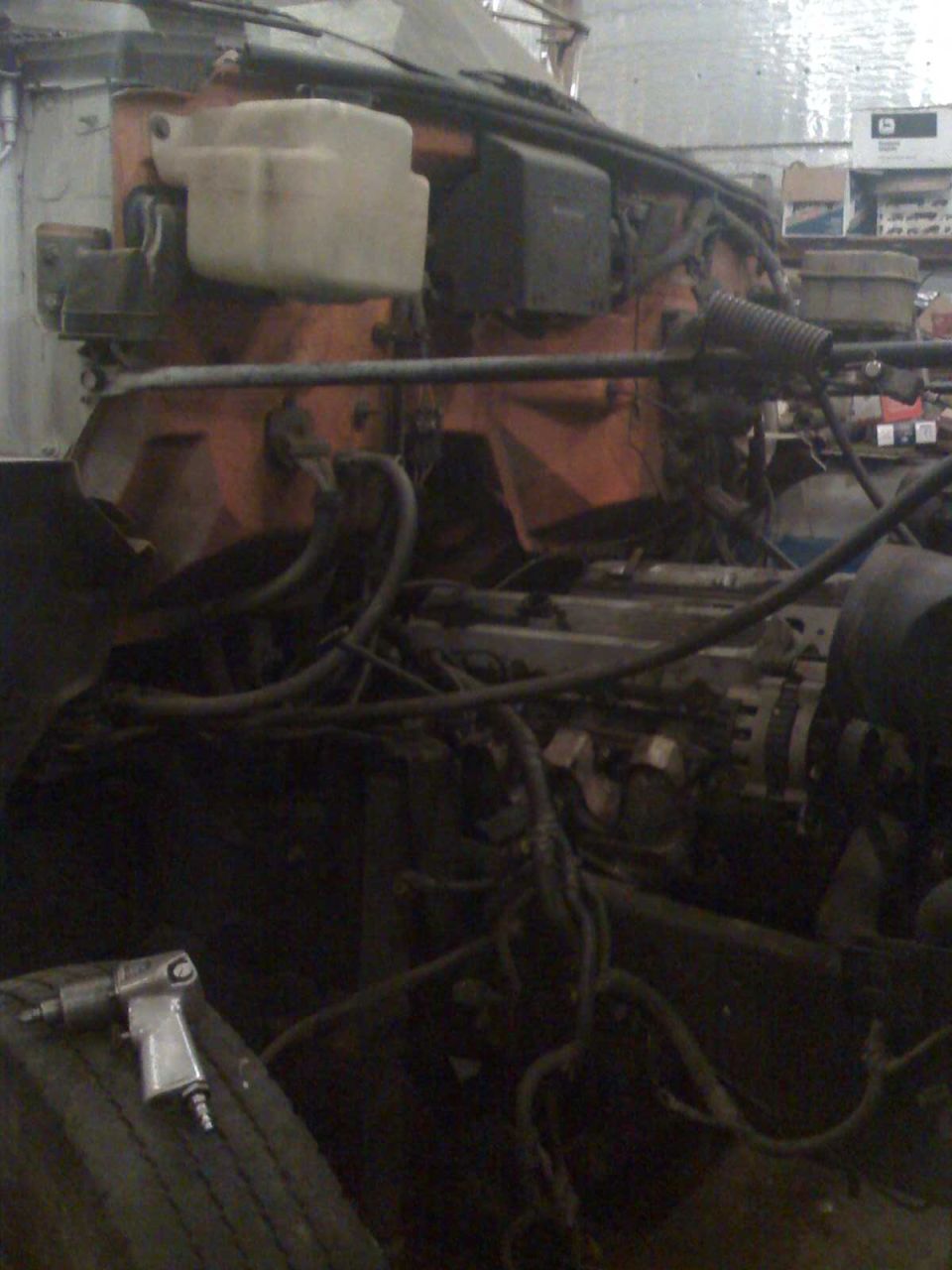 Air impact wrench on tire next to truck engine bay with hoses and components