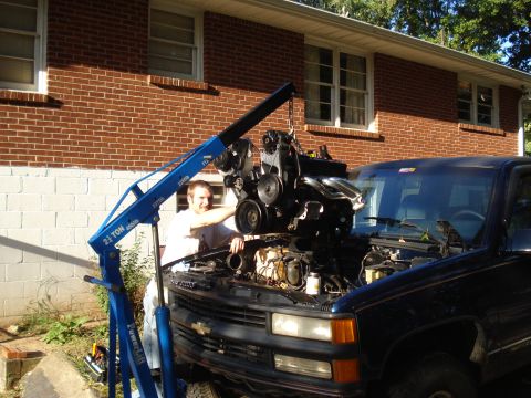 1984 Jeep J-10 - An engine is being removed from a dark blue pickup truck using a blue engine hoist.