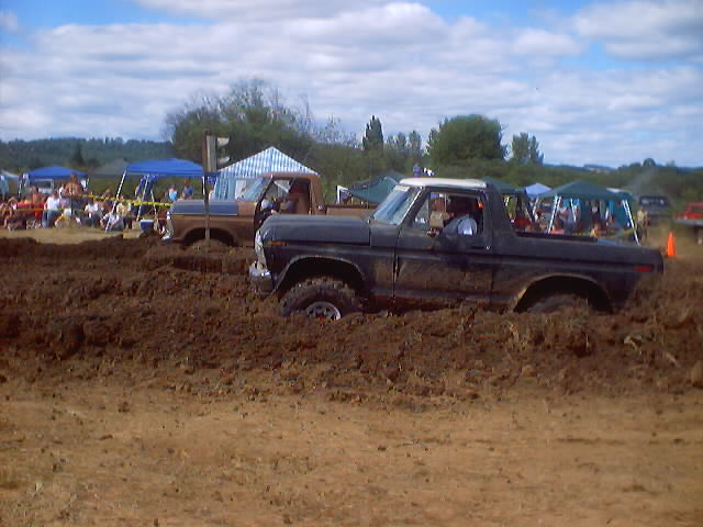 Black Ford F-Series truck stuck in mud, white roof, driver visible