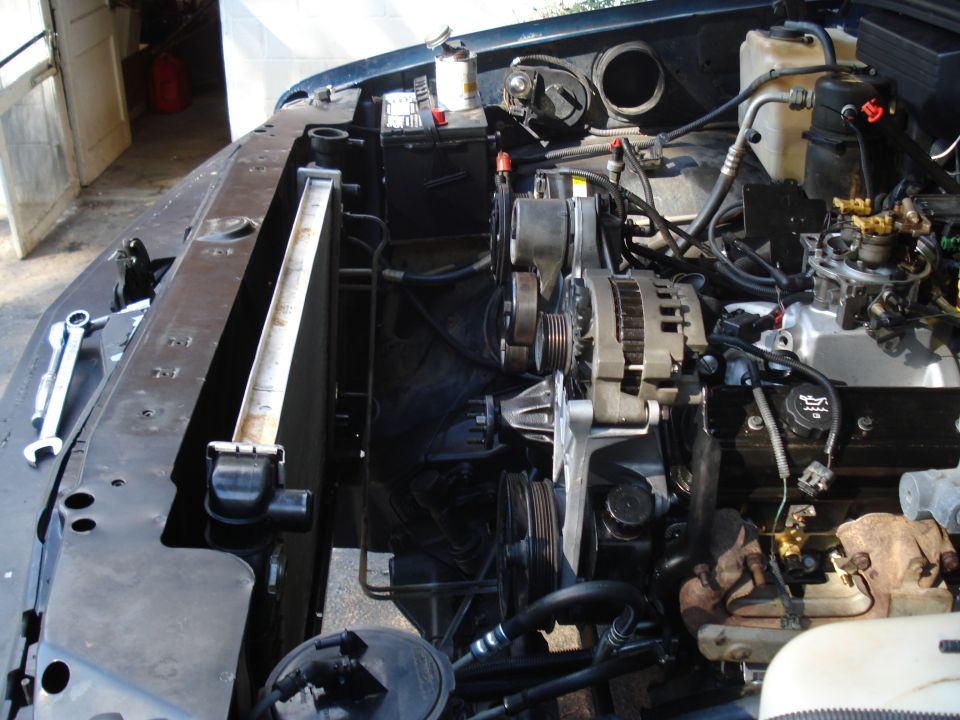 Engine bay with radiator, alternator, and engine components visible. Tools are on the left
