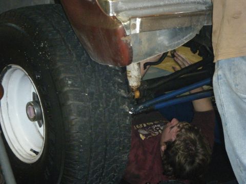 1979 Ford Bronco - Two people are working on the underside of a vehicle, with a focus on the suspension and tire area.