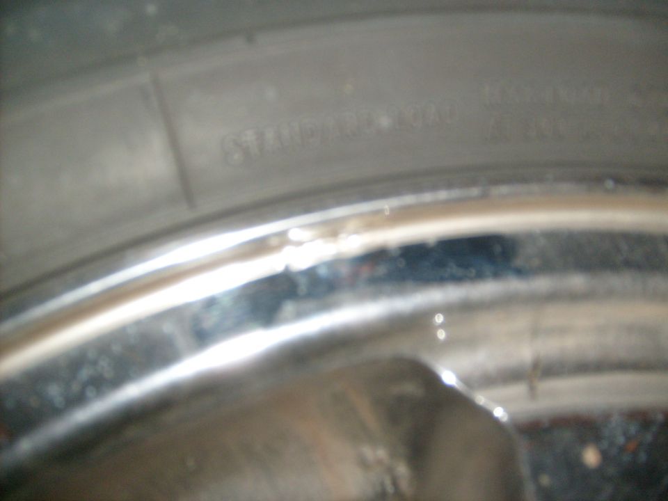 Blurry close-up of a tire sidewall marked STANDARD LOAD against a chrome wheel lip