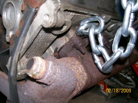 1995 Mercury Grand Marquis - A chain is attached to a rusty exhaust manifold, suggesting an engine is being prepared for removal or installation.