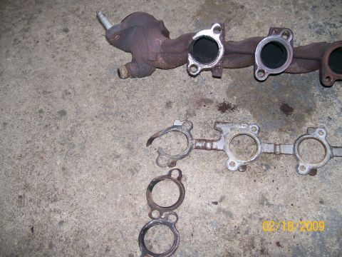 1995 Mercury Grand Marquis - Exhaust manifold and gaskets are shown on a concrete surface, likely after removal from a vehicle.