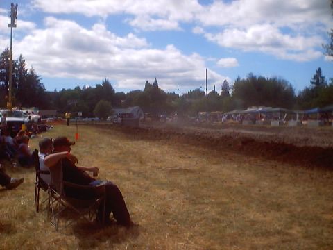 1976 Ford F-100 - Spectators watch a mud drag race event on a sunny day with clouds in the sky.
