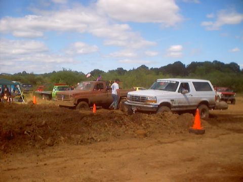 1976 Ford F-100 - Vehicles are stuck in the mud during a competition, with spectators in the background.