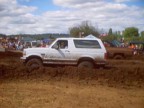 1976 Ford F-100 - A white Ford Bronco navigates a muddy track during a competition, likely, off-road event.