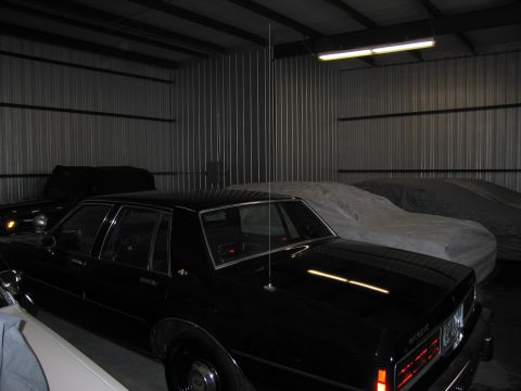 1991 Ford LTD Crown Victoria - Photograph of a black sedan stored alongside covered cars in a warehouse, not a technical document.