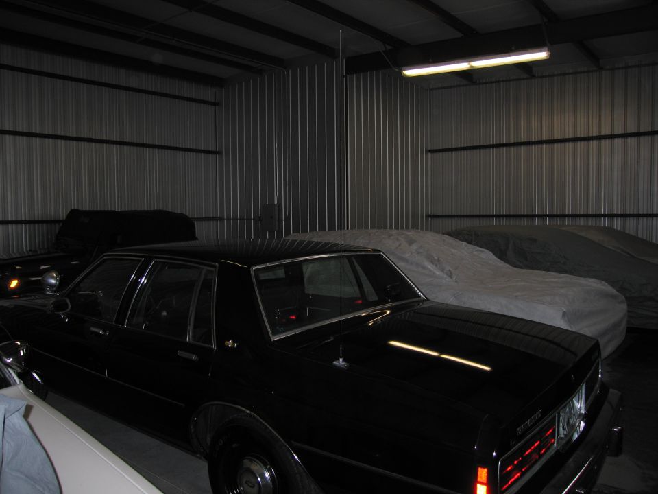 Black sedan parked among covered cars in a metal storage building