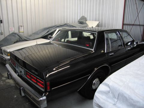 1991 Ford LTD Crown Victoria - Photograph of a black Chevrolet Caprice sedan stored with covered vehicles, not a technical document.