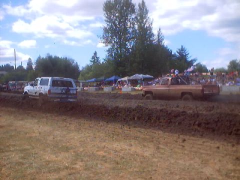 1976 Ford F-100 - Two trucks compete in a mud race event with spectators in the background.