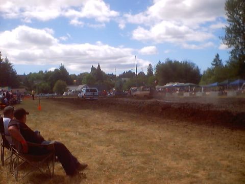 1976 Ford F-100 - Spectators watch a mud drag race event on a sunny day with scattered clouds.