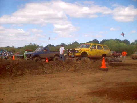 1976 Ford F-100 - Two vehicles are stuck in the mud at an outdoor event, with spectators in the background.