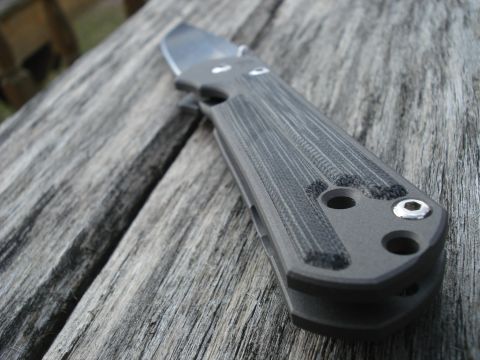 2000 Ford Crown Victoria - A close-up, angled shot of a folding knife with a gray textured handle resting on a weathered wooden surface.