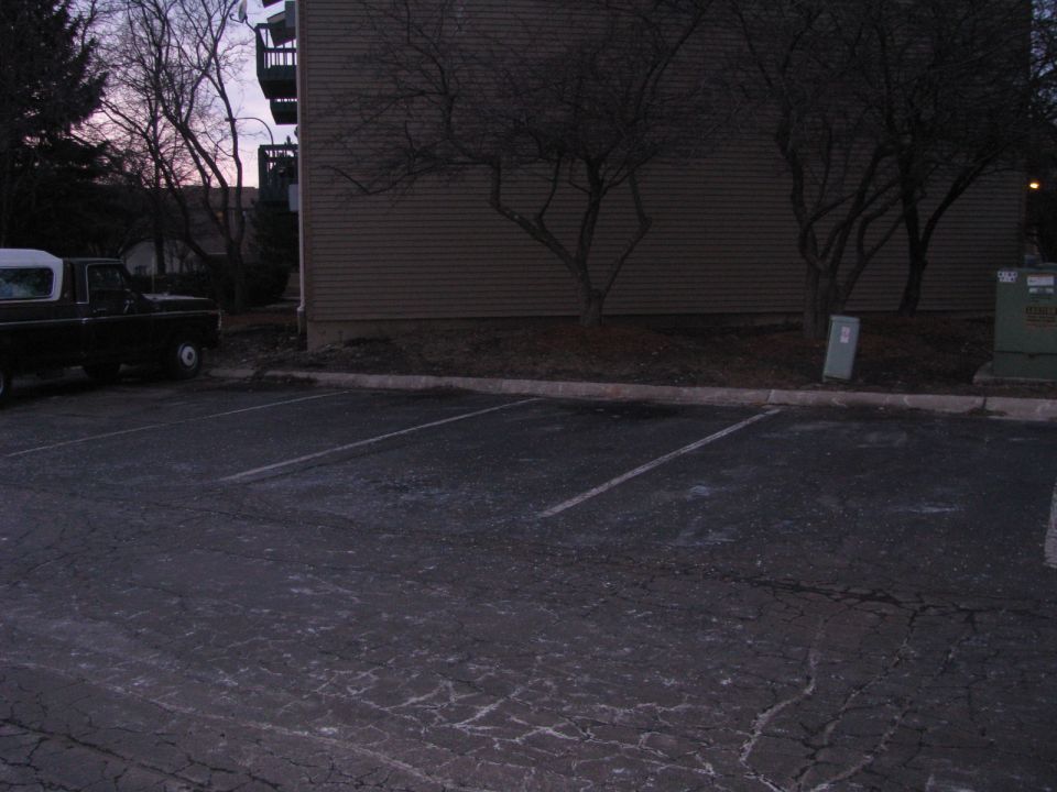 Side view of black pickup truck with white camper shell parked in lot