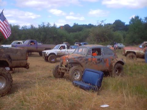 1976 Ford F-100 - A heavily modified Volkswagen Beetle sits in a muddy field alongside several trucks, likely at a mud drag event.