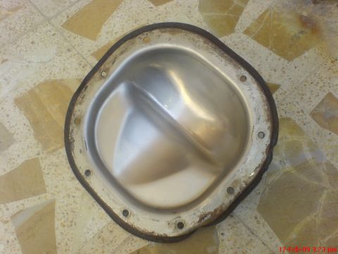 1992 Ford Crown Victoria - A shiny metal differential cover with a dark, rusty gasket is shown from a top-down view, resting on a tiled floor.