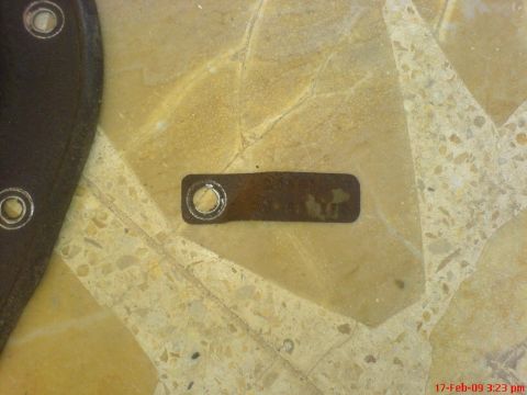 1992 Ford Crown Victoria - A close-up view of a small, rectangular metal tag with a hole punched through it, lying on a speckled, beige and yellow tiled floor. The ta…