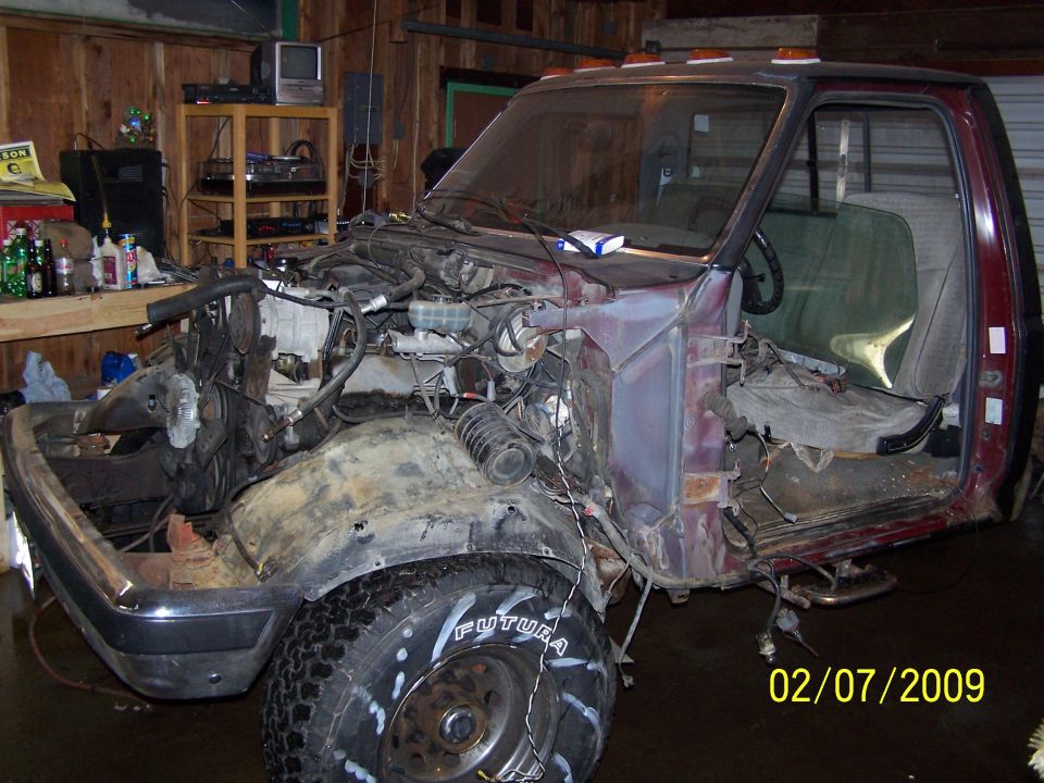 Maroon Ford F-250 pickup truck in a garage, disassembled with engine exposed.