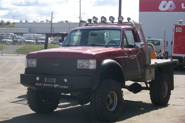 Lifted dark red Ford F-250 pickup truck with flatbed and off-road tires.