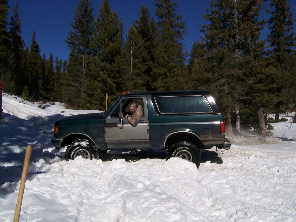 1990 Ford Bronco driving through snow in a wooded area.