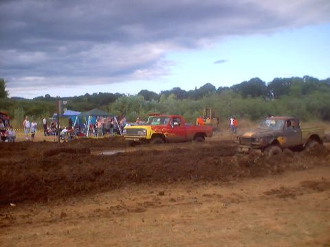 1976 Ford F-100 - Trucks are stuck in the mud during a competition, with a crowd watching under cloudy skies.