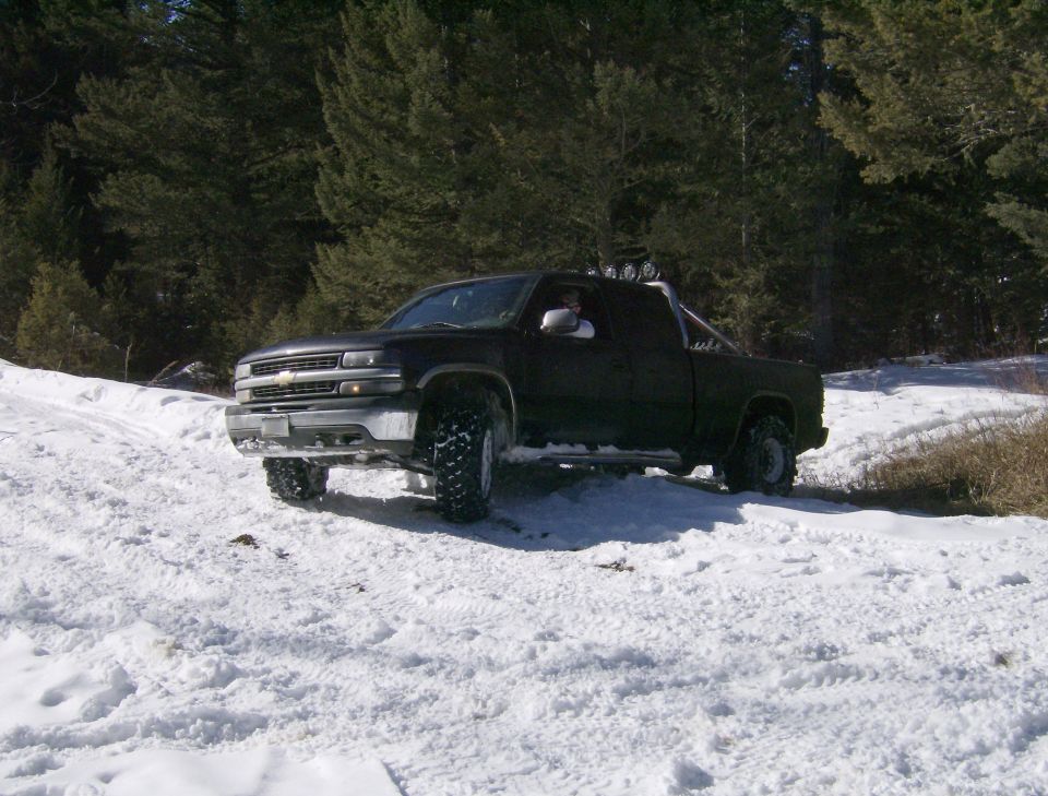 Black pickup truck with off-road tires in a snowy forest setting.