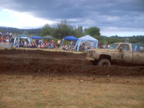 1976 Ford F-100 - A muddy truck navigates a challenging course at a drag race event with spectators in the background.