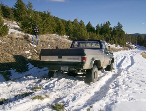1990 Ford Bronco - A silver and black Chevrolet pickup truck is parked on a snowy, unpaved road with tire tracks visible in the snow. A person wearing jeans a…